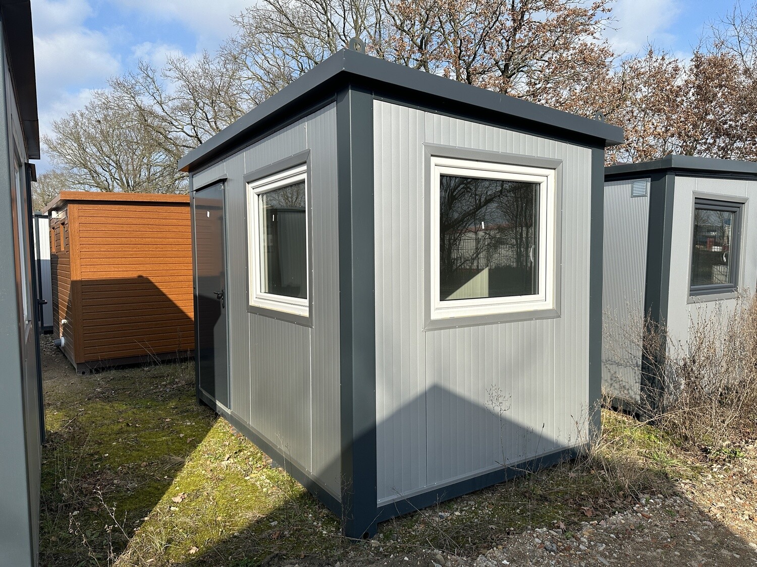 Zwischen weiteren Einheiten aufgestellter Bürocontainer 3,50 x 2,20 m mit zwei hellen Fenstern