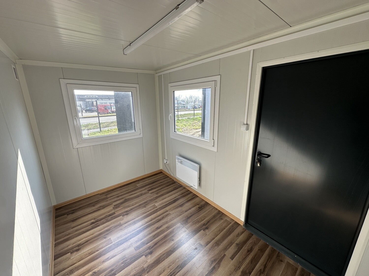 Innenansicht des Bürocontainers 3,50 x 2,20 m: zwei Fenster, Wandheizgerät und dunkle Außentür