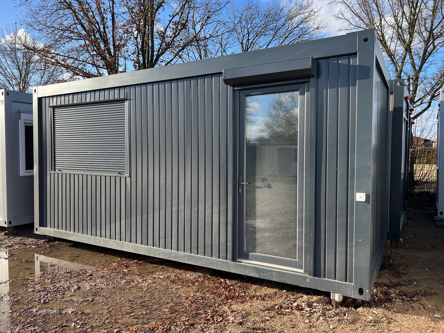 Heruntergelassener Rollladen vor dem Fenster neben der Glastür des Bürocontainers 6,00 x 2,44