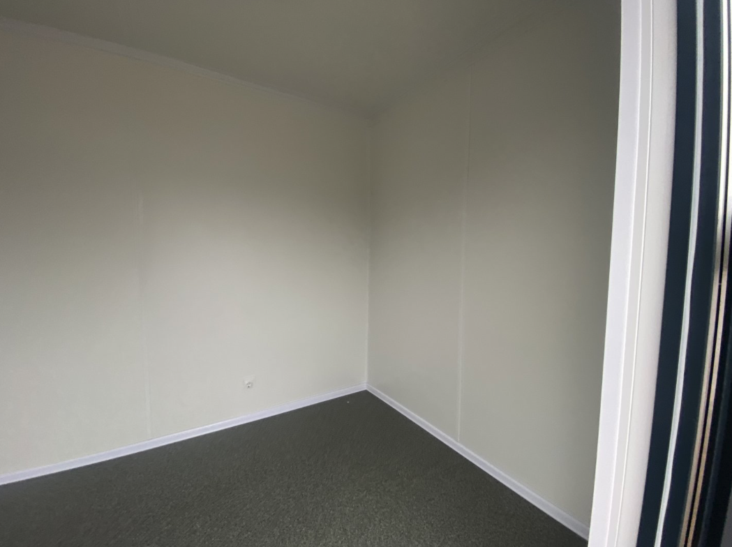 Leerer Innenraum mit dunkelgrauem Bodenbelag und weißen Wandpaneelen, Bürocontainer 6,00 x 2,44