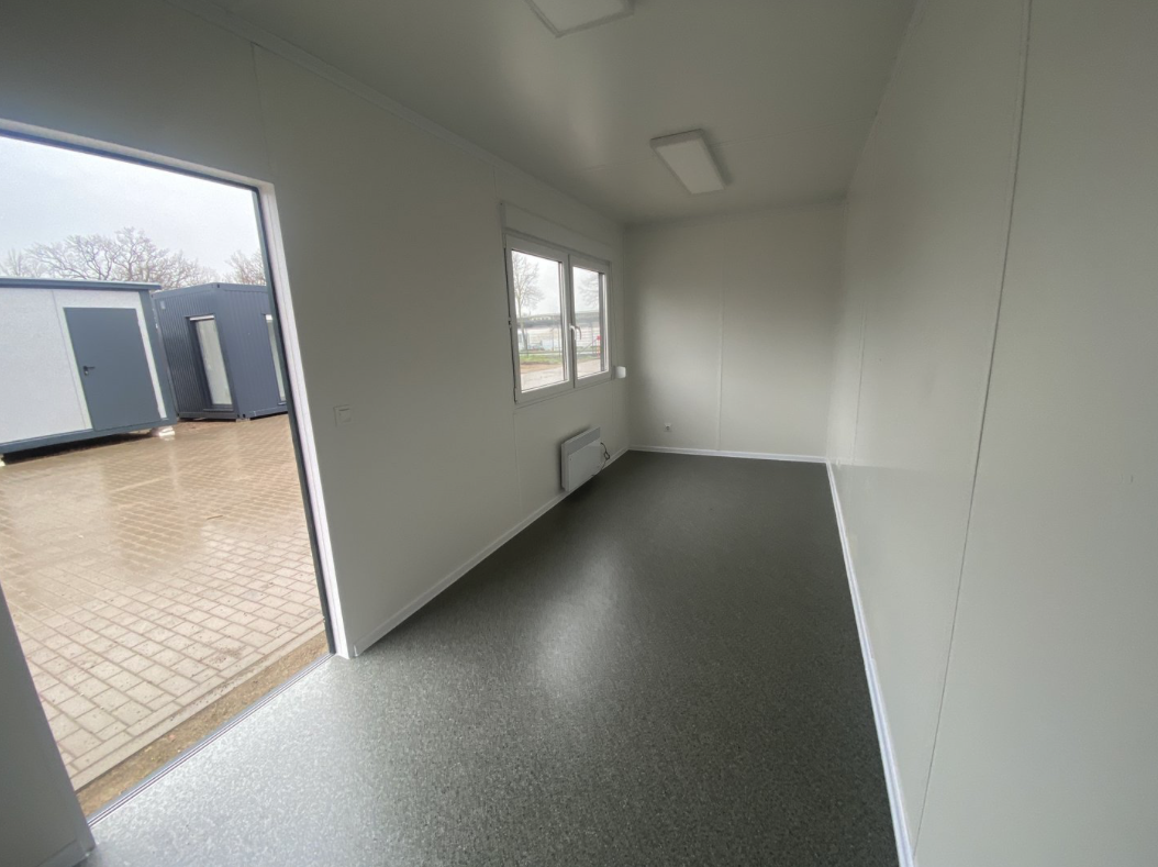 Durch die offene Tür fällt Licht in den Bürocontainer 6,00 x 2,44 mit Fenster und Wandheizgerät