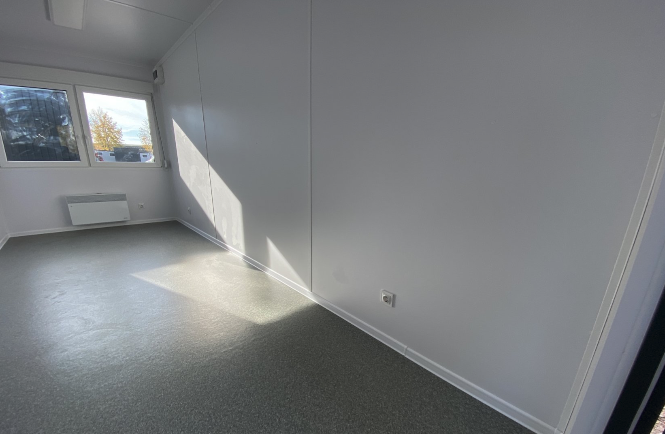 Blick in die Ecke des Bürocontainers: glatte helle Wandpaneele, Steckdose und grauer Boden