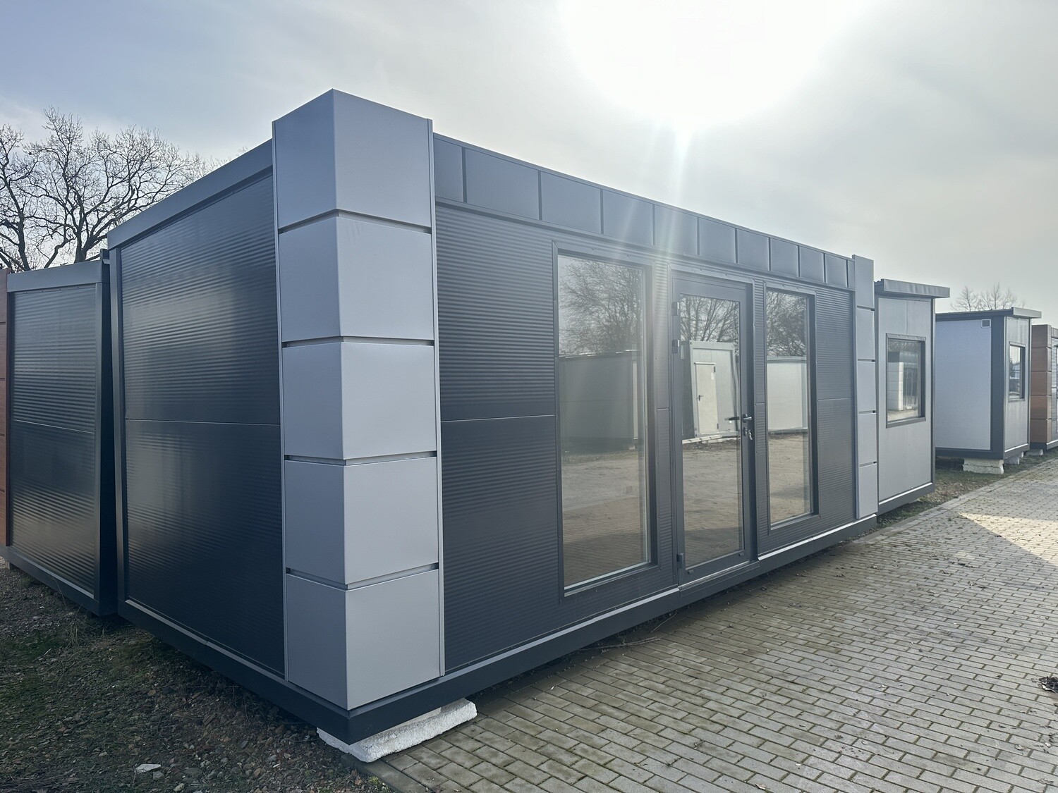 Über Eck fotografierter Bürocontainer 6,00 x 2,80 m in Anthrazit mit hellgrauen Eckpaneelen und Glasfront