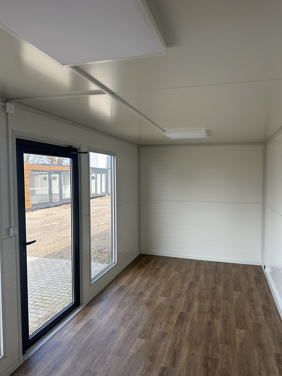 Innenraum mit Laminatboden in Holzoptik, weißen Wänden, verglaster Tür und Deckenleuchte