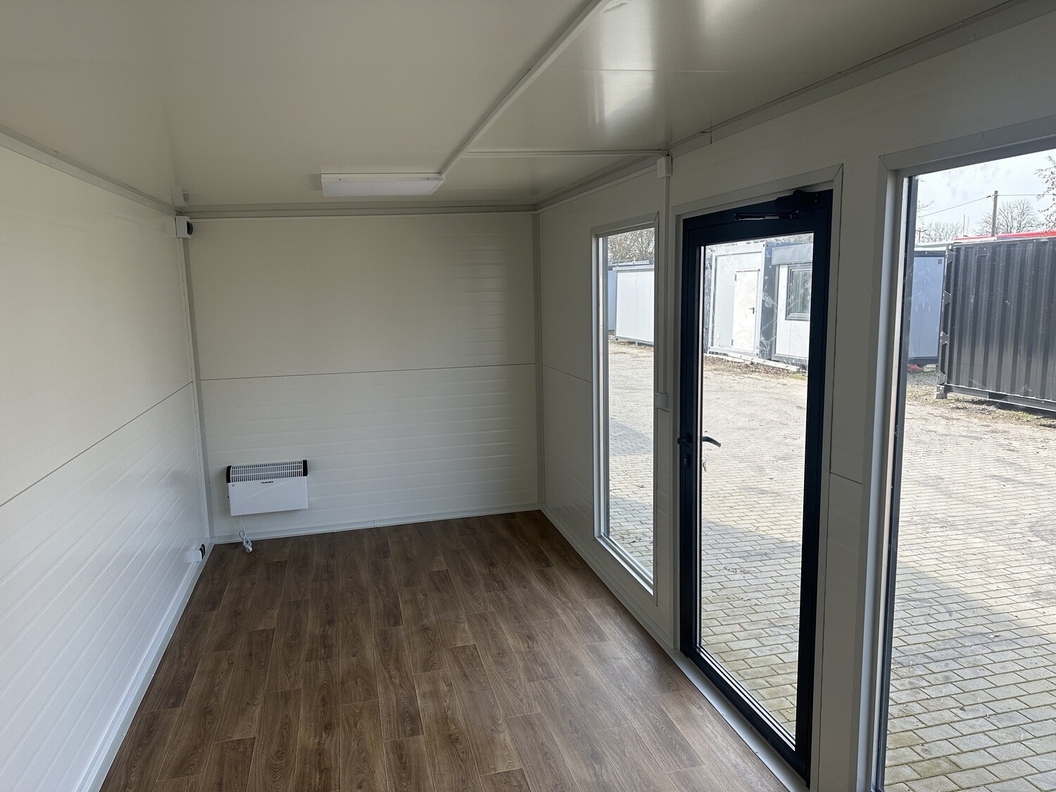 Blick in den leeren Büroraum mit Wandheizgerät, Holzoptikboden und raumhoher Verglasung