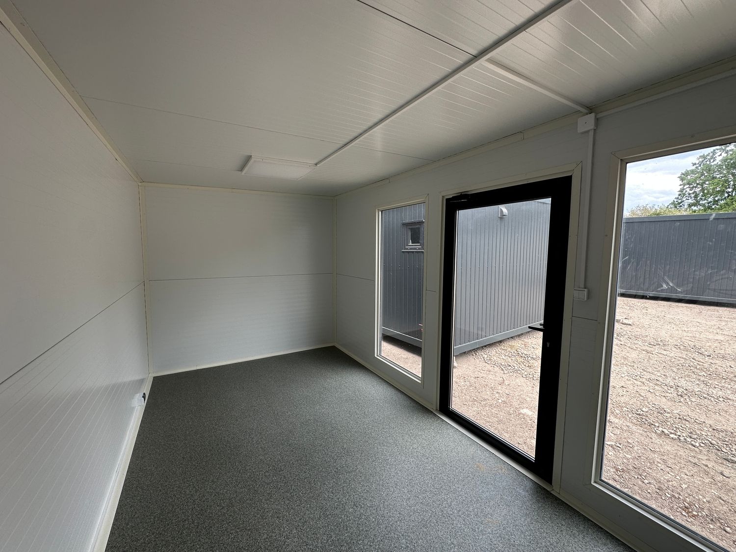 Eckperspektive des Innenraums mit hellen Wänden, grauem Boden, Fixfenster und Glastür