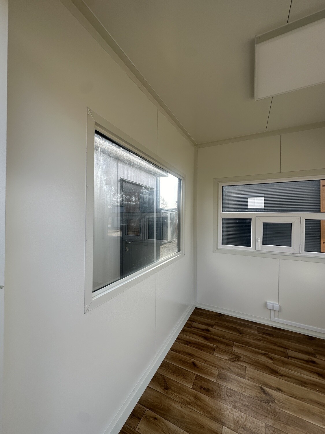 Innenansicht mit großem Fenster, Rollladenfenster, Boden in Holzoptik und heller Wandverkleidung