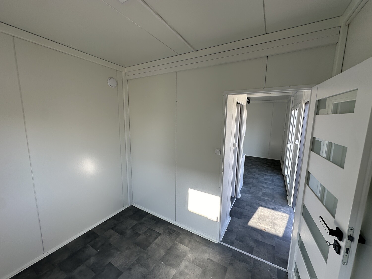 Blick aus einem Zimmer durch die Tür mit Glasstreifen in den Flur der Tromsø mit grauem Boden