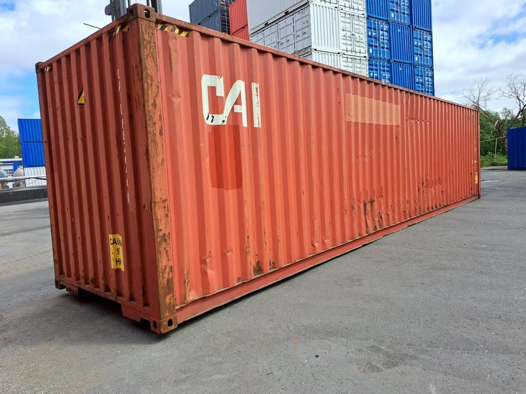 Längsseite und Stirnwand des Lagercontainers mit Rostspuren, dahinter gestapelte Seecontainer