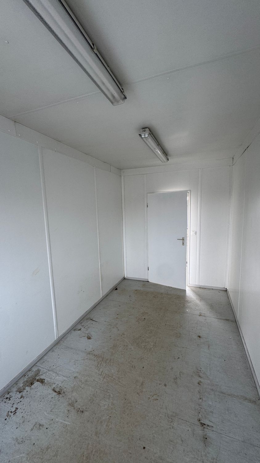 Blick durch den leeren Büroraum auf die weiße Innentür, Wandpaneele und Deckenleuchten