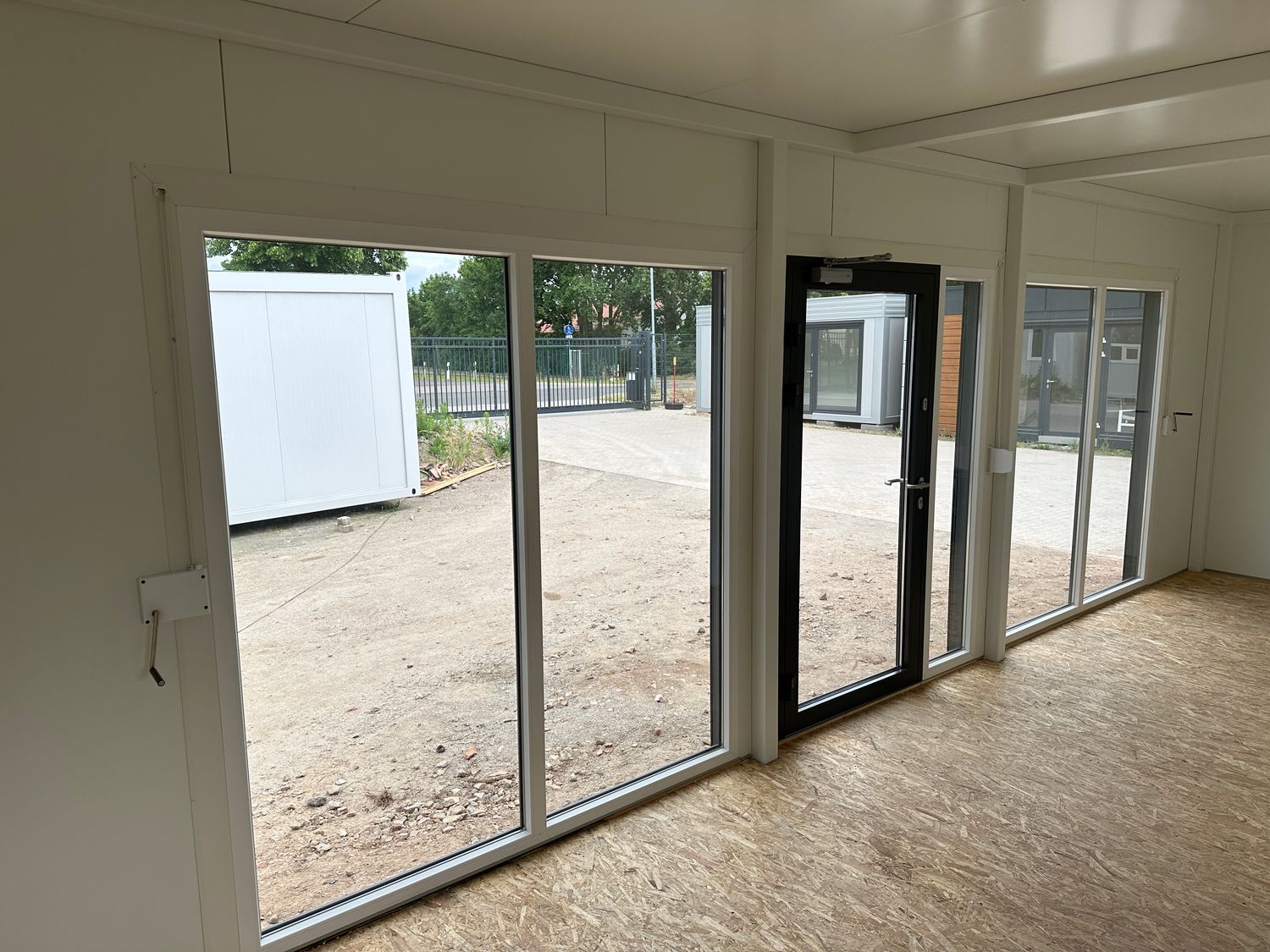Innenansicht mit raumhoher Fensterfront, dunkler Glastür und OSB-Boden im Imbisscontainer