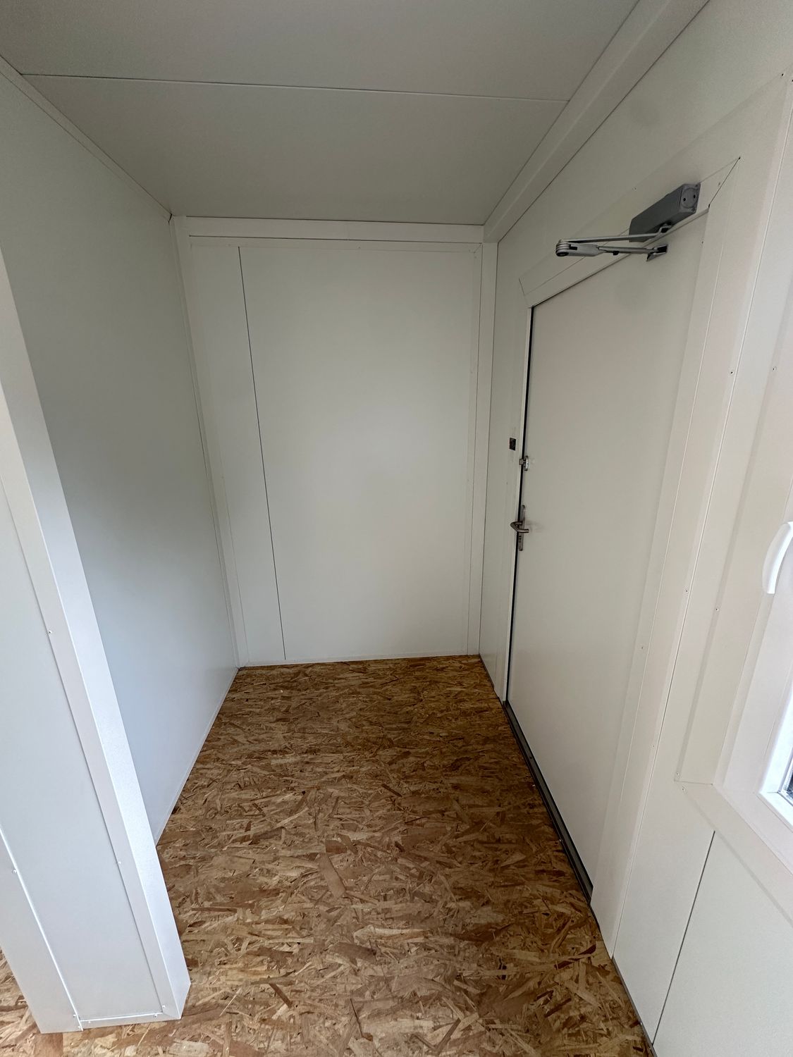 Kleiner Vorraum mit weißer Tür, Türschließer und OSB-Boden im Imbisscontainer 5,00 x 8,00