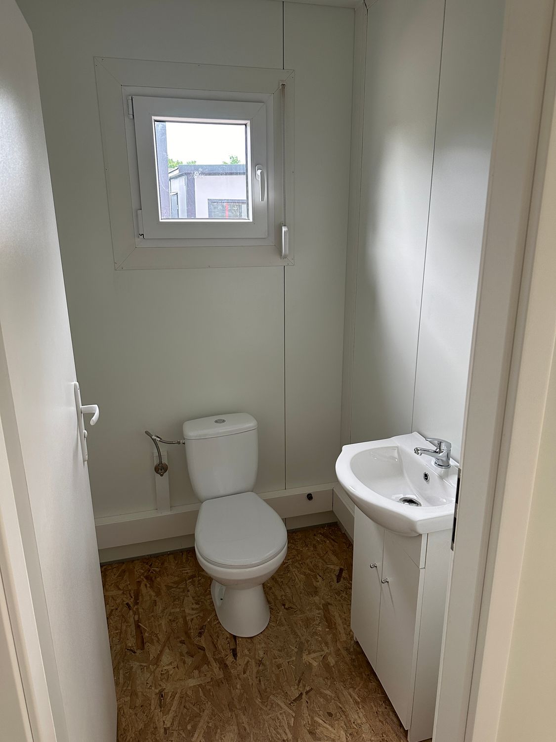Zweiter WC-Raum mit Toilette, Waschtisch und Papierhalter neben dem Fenster im Imbisscontainer