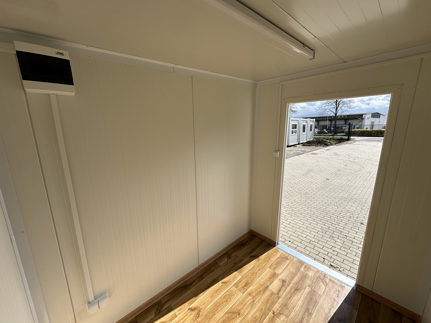 Blick durch die geöffnete Tür des Lagercontainers nach draußen, links ein Sicherungskasten