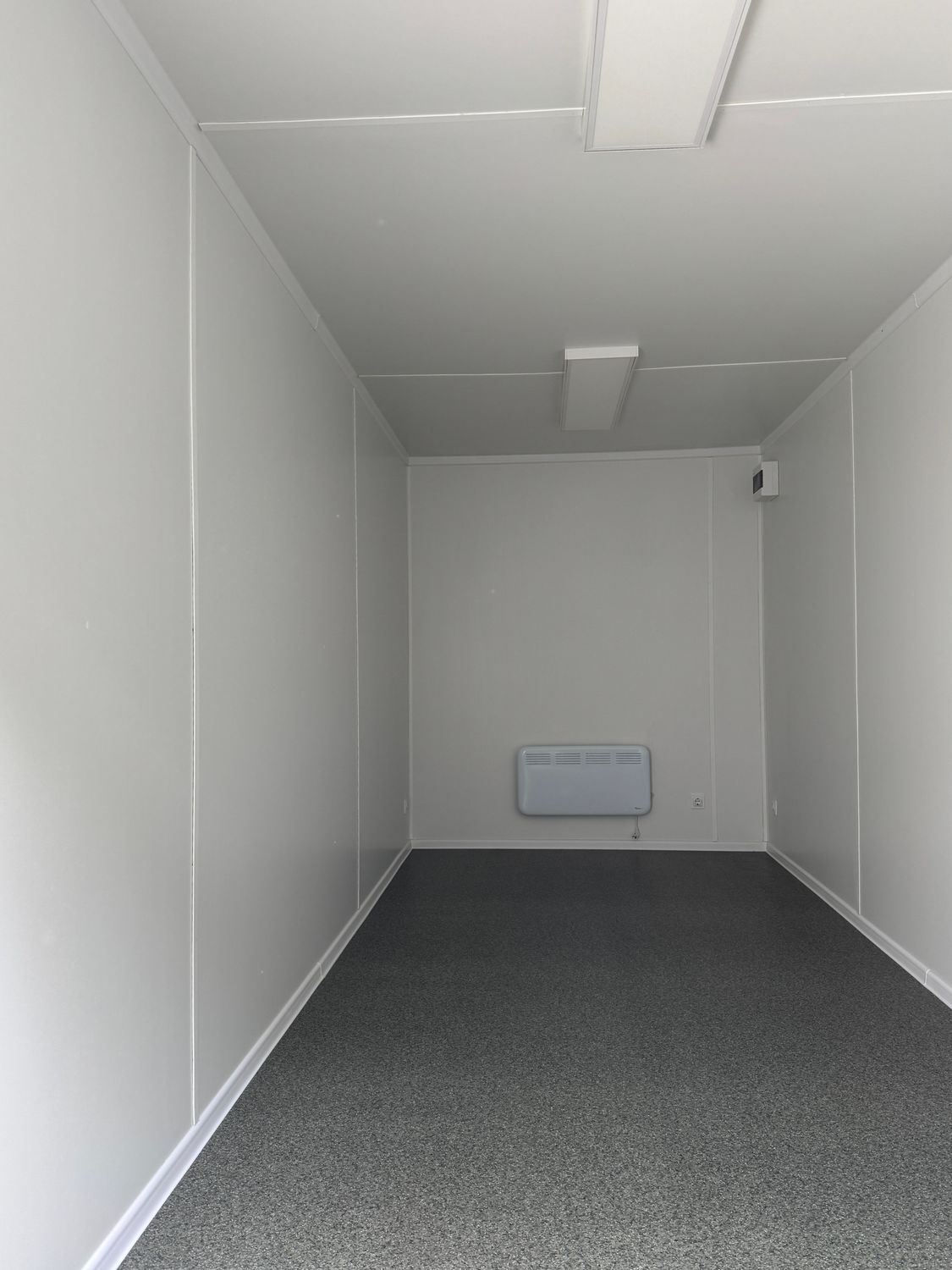 Innenansicht mit weißen Wänden, grauem Bodenbelag, Wandheizgerät und zwei Deckenleuchten