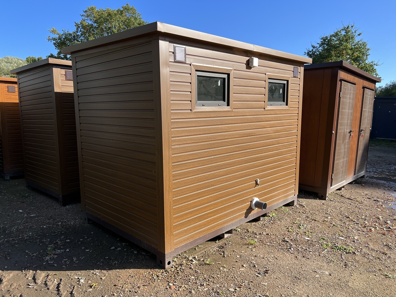 Rückseite mit zwei kleinen Fenstern, Lüftungsgitter und Abwasserstutzen am Premium Doppel-WC Container