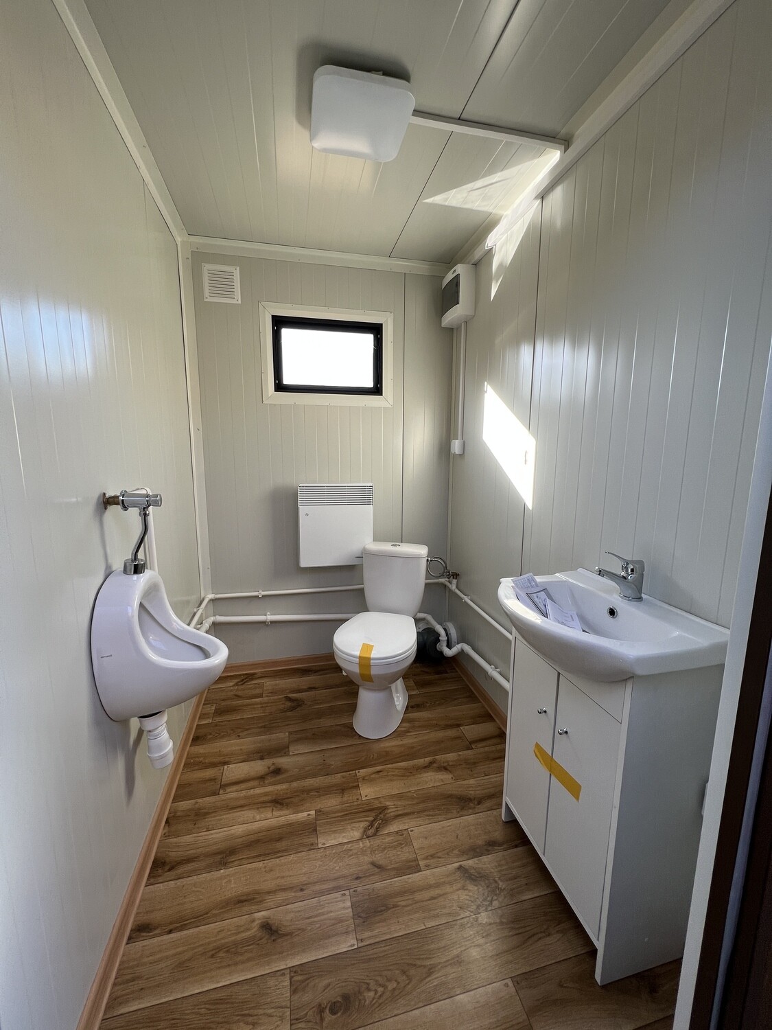 Innenansicht mit Urinal, WC, Waschtisch und Wandheizkörper über Holzdekor-Boden im Doppel-WC Container