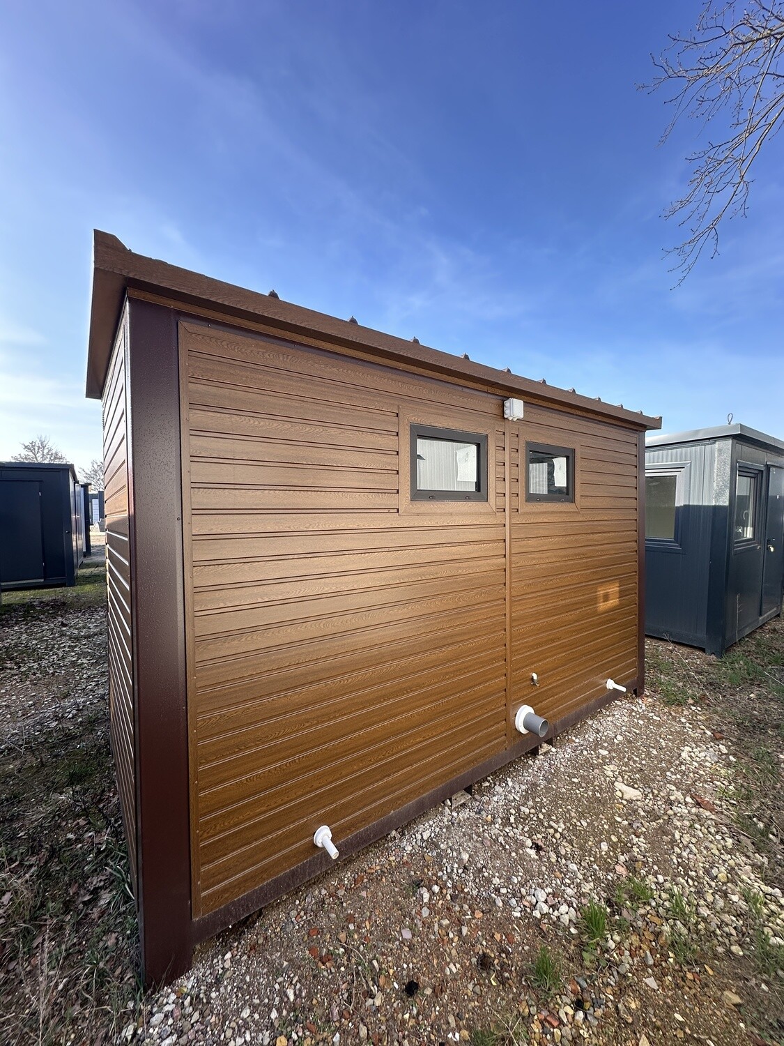 Rückansicht mit zwei kleinen Fenstern und weißen Abwasserstutzen an der Wand in Holzoptik