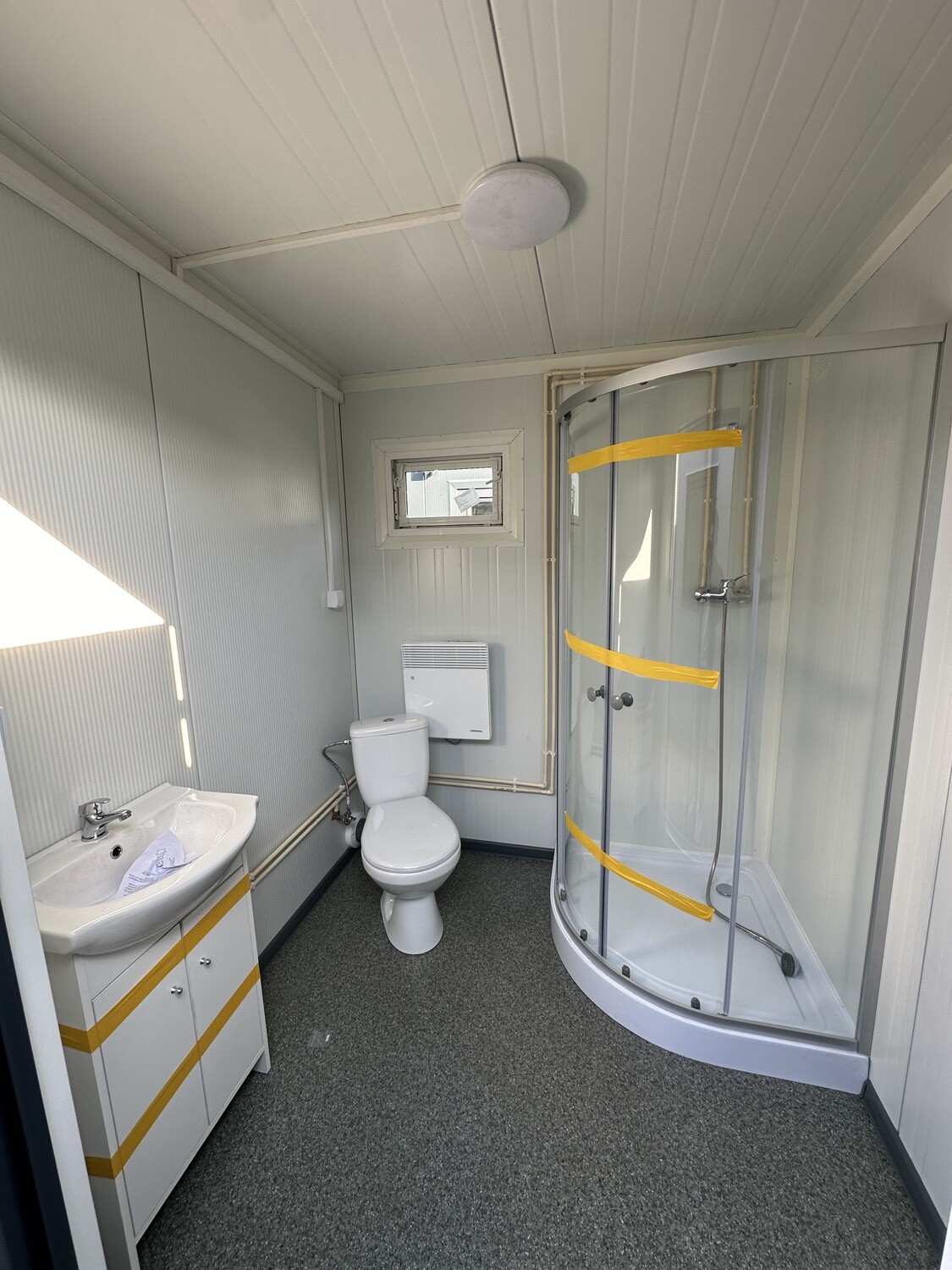 Waschtisch, Toilette und Eckdusche nebeneinander im Duschcontainer in Holzoptik, mit Fenster