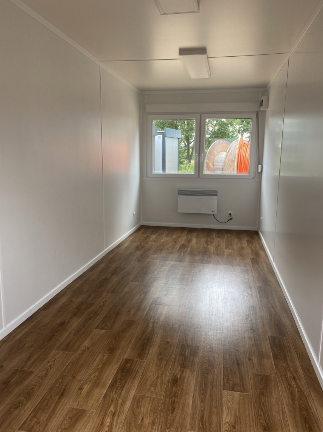Innenraum mit Fenster, Wandkonvektor und dunklem Holzdekor-Boden zwischen weißen Wandpaneelen