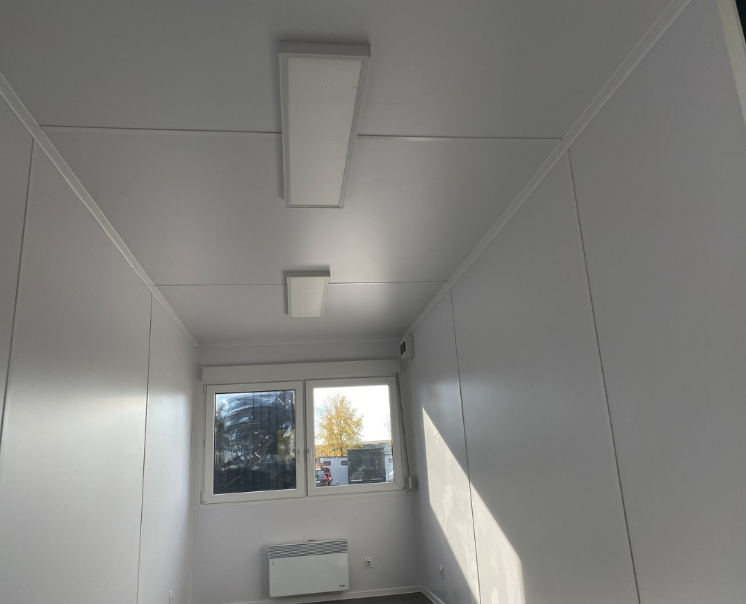 Deckenbereich mit zwei LED-Leuchten, darunter Fenster und Konvektor an der Stirnwand des Büros