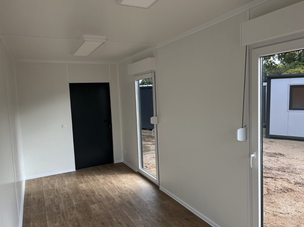 Blick zur schwarzen Innentür, daneben zwei Glastüren und helle Wandpaneele über Laminatboden