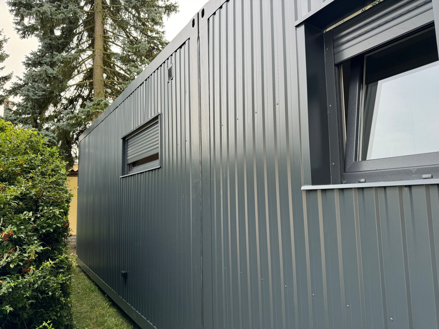 Detailaufnahme der anthrazitfarbenen Trapezblechwand mit Rollladenfenster und geöffnetem Kippfenster