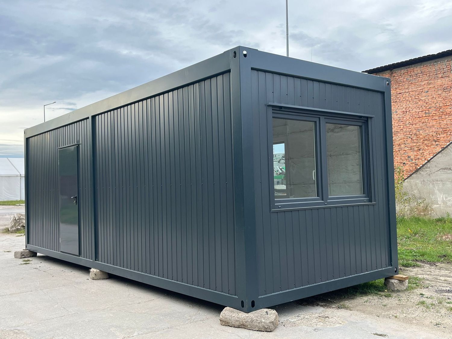 Stirnseite mit Fenster und angrenzende Längswand mit Eingangstür des Wohncontainers