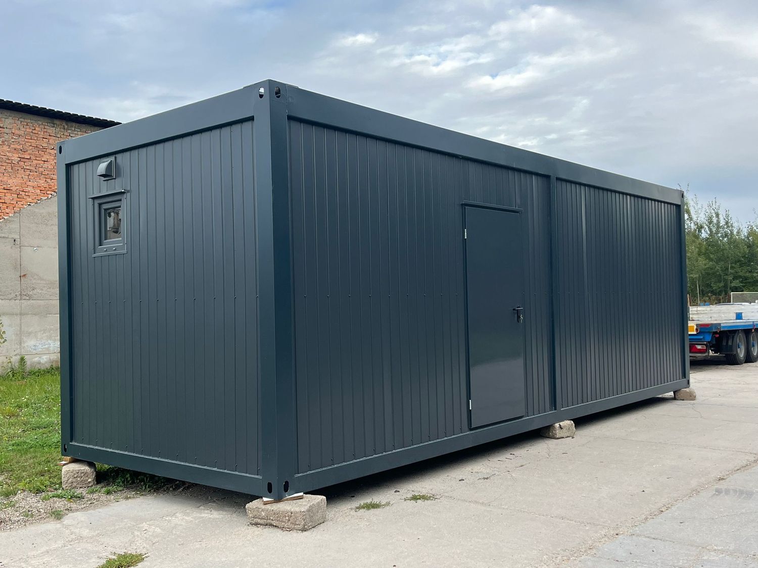 Rückansicht des Wohncontainers mit kleinem Fenster, Außenleuchte und Tür in der Längswand