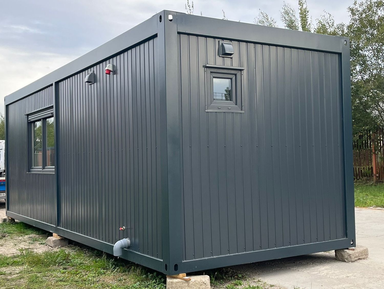 Schmalseite des Wohncontainers mit Lüftungsgitter, kleinem Fenster und rotem CEE-Anschluss