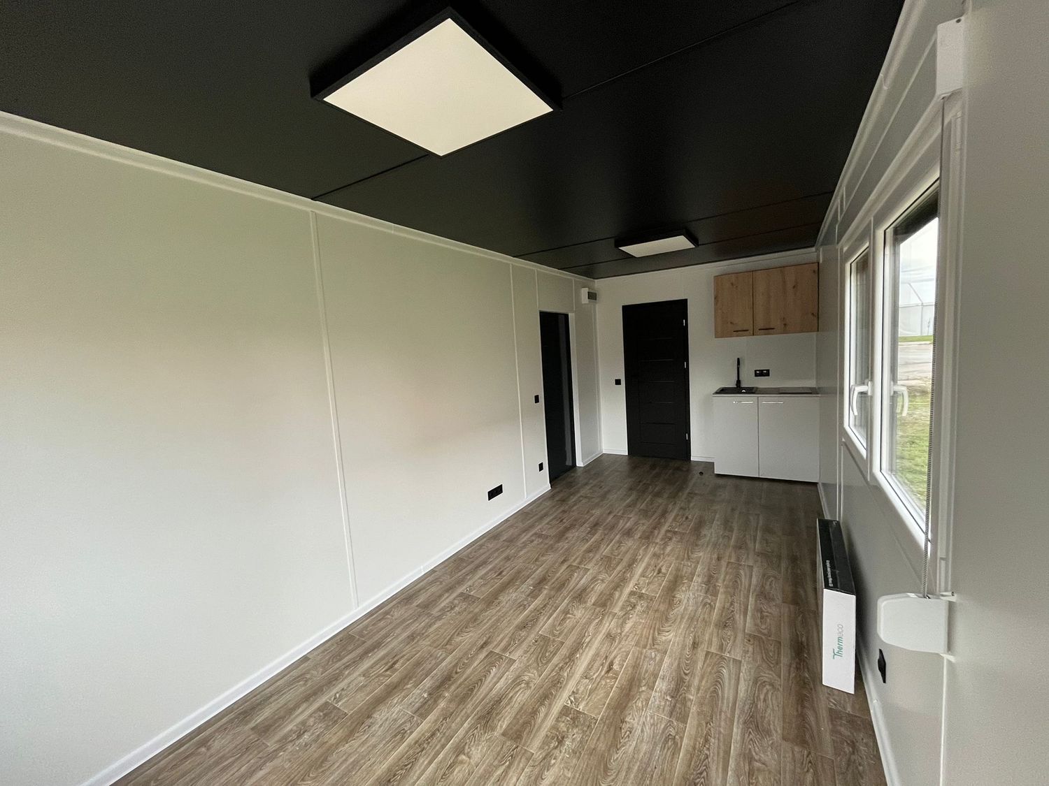 Innenansicht des Wohnraums mit Holzoptik-Boden, dunkler Decke, LED-Panel und Küchenzeile