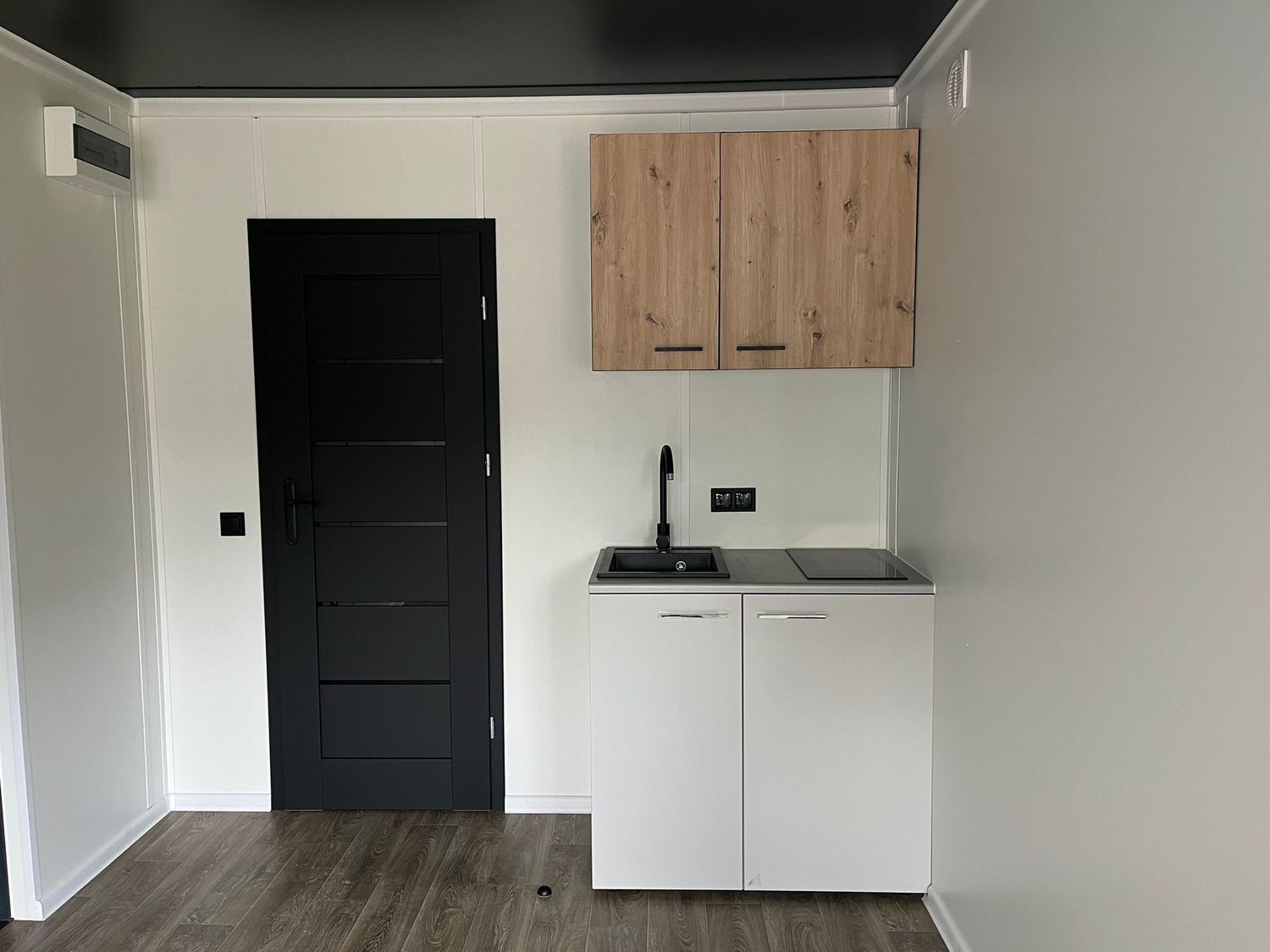 Küchenzeile mit Hängeschrank in Holzoptik, Spüle, schwarzer Armatur und dunkler Zimmertür