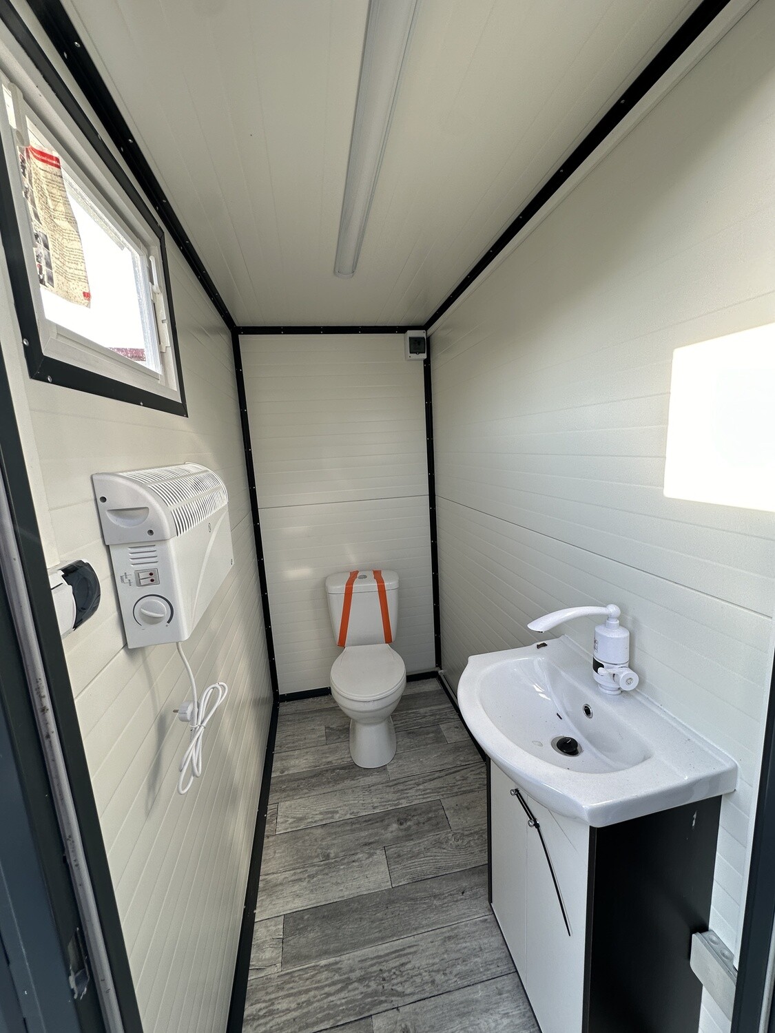 Innenraum mit WC, Waschtisch, Wandkonvektor und Fenster im Sanitärcontainer 2,00 x 1,15 m