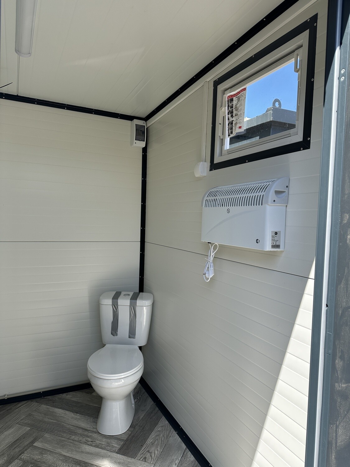 Blick in die WC-Ecke mit Wandkonvektor, Fenster und Fischgrätboden, Sanitärcontainer 2,00 x 2,00 m
