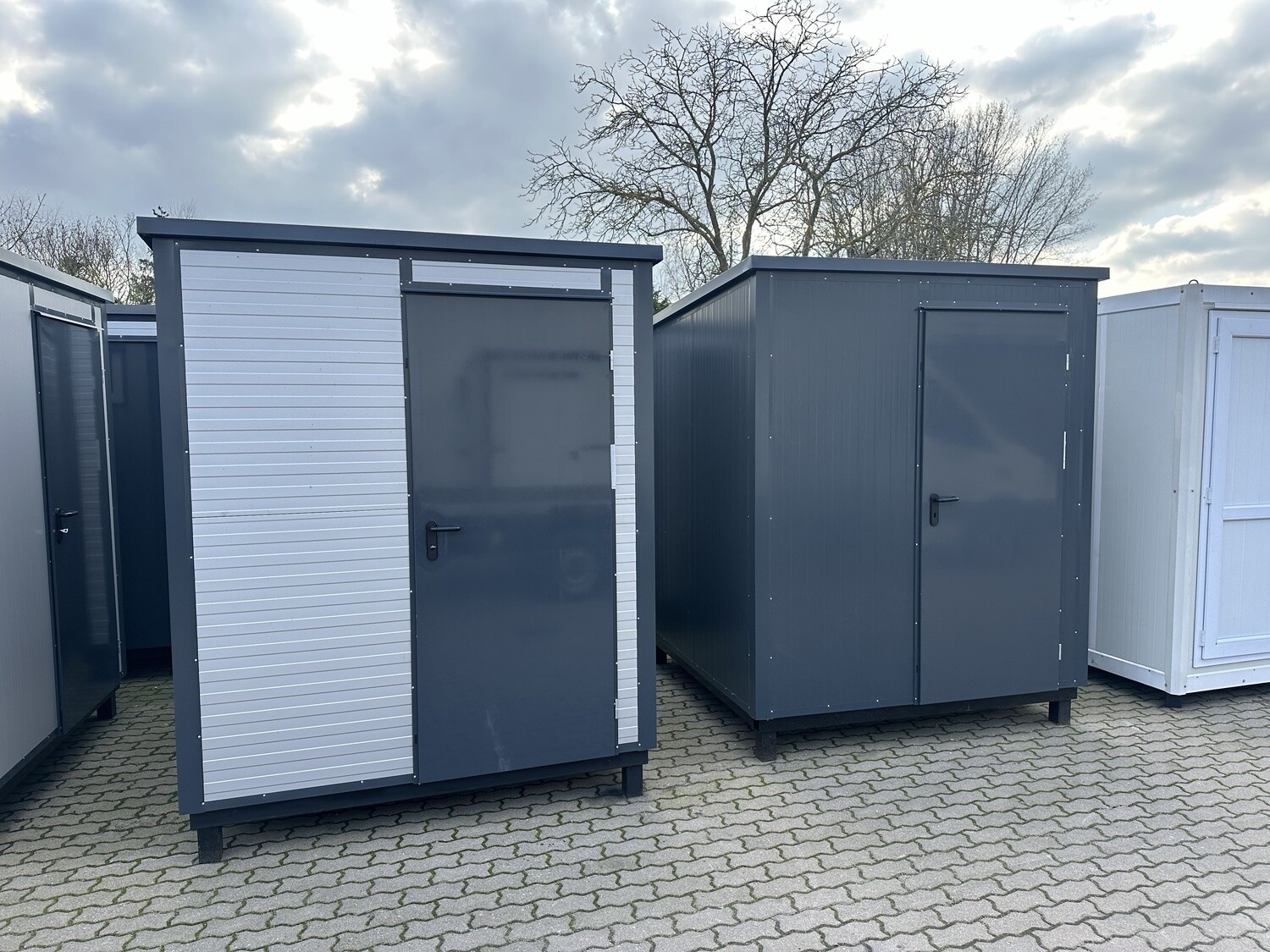 Zwei aufgestellte Sanitärcontainer 2,00 x 2,00 m, einer hell verkleidet, einer in Anthrazit