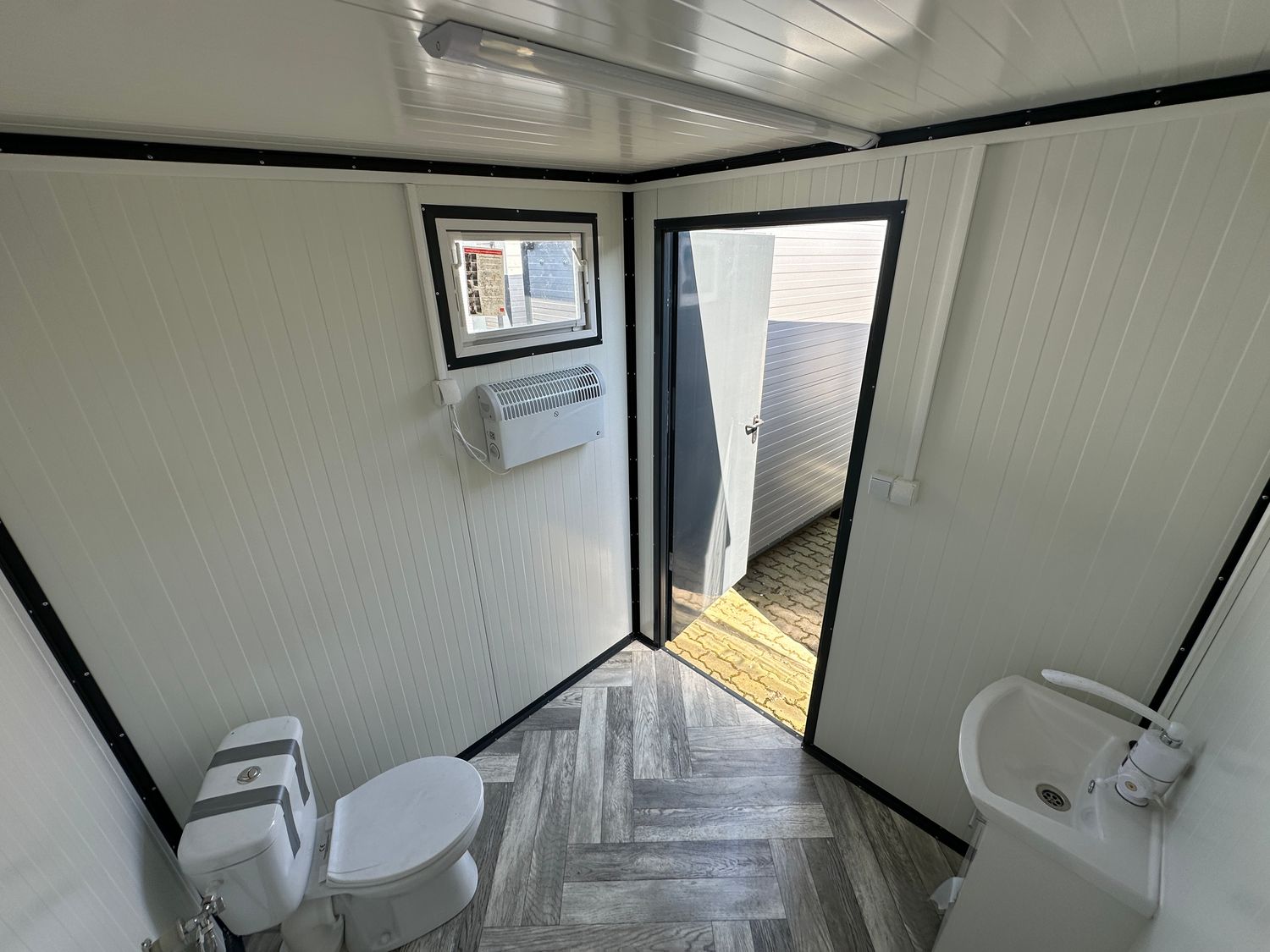 Von innen zur offenen Tür fotografiert: WC, Handwaschbecken, Fenster und Heizgerät an der Wand