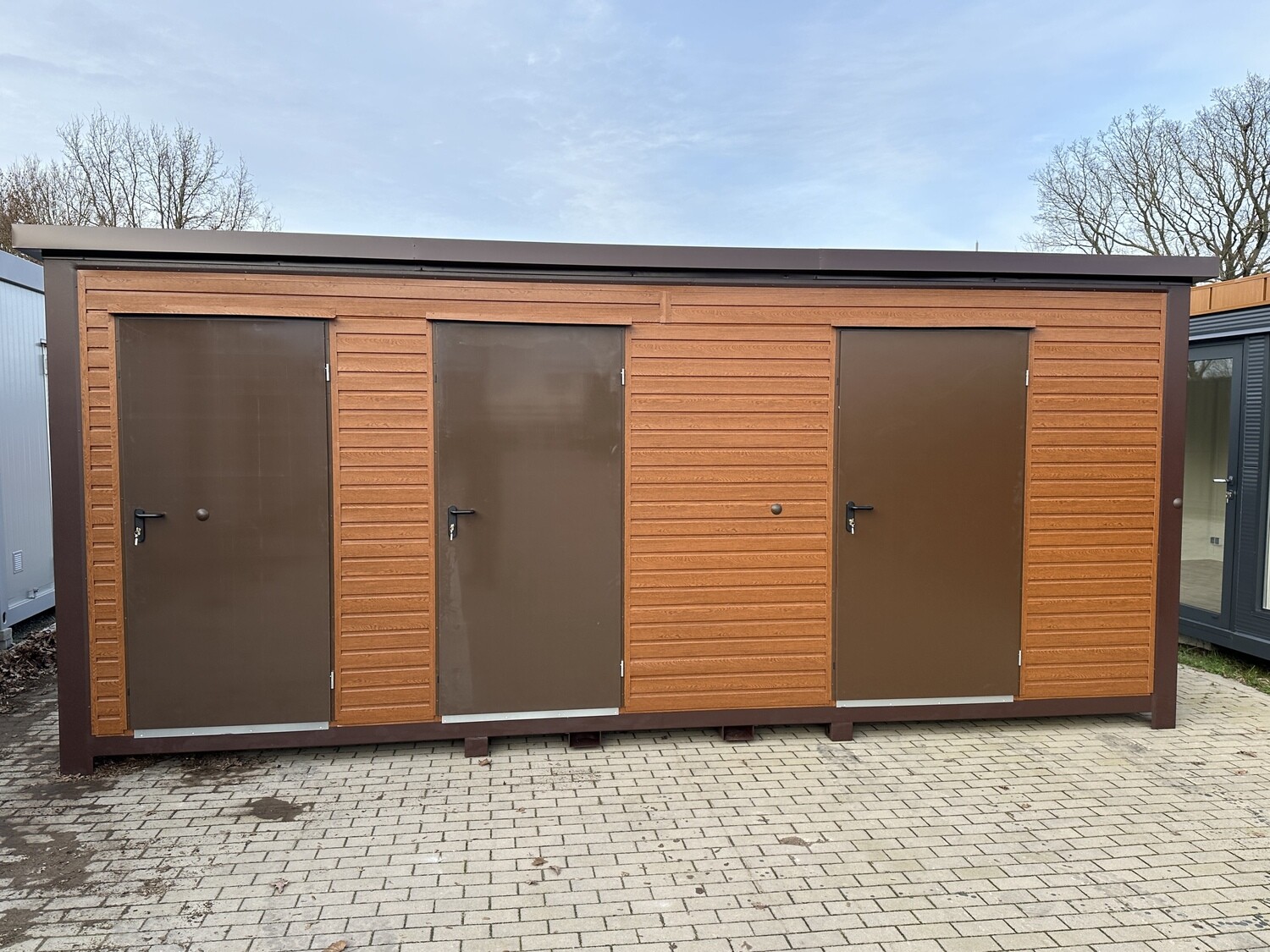 Holzoptik in Braun: andere Ausführung mit drei Türen, frontal auf gepflasterter Fläche aufgenommen