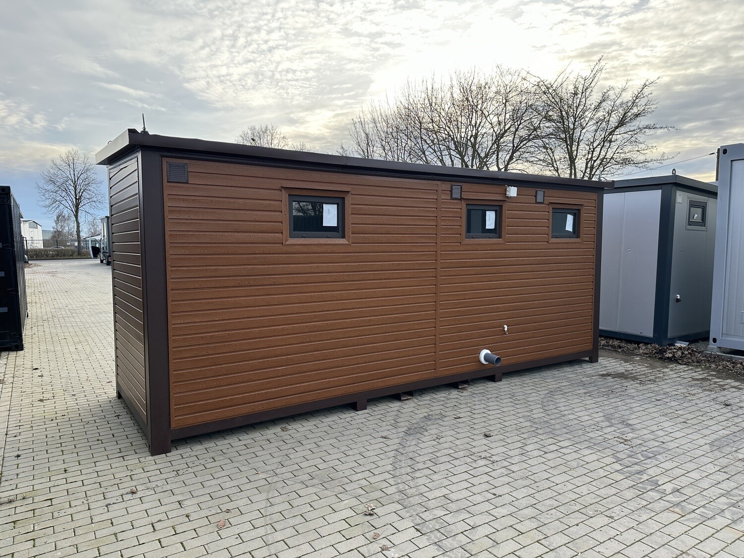 Schräge Rückansicht der braunen Holzdekor-Ausführung mit Fenstern und seitlichem Abwasserrohr
