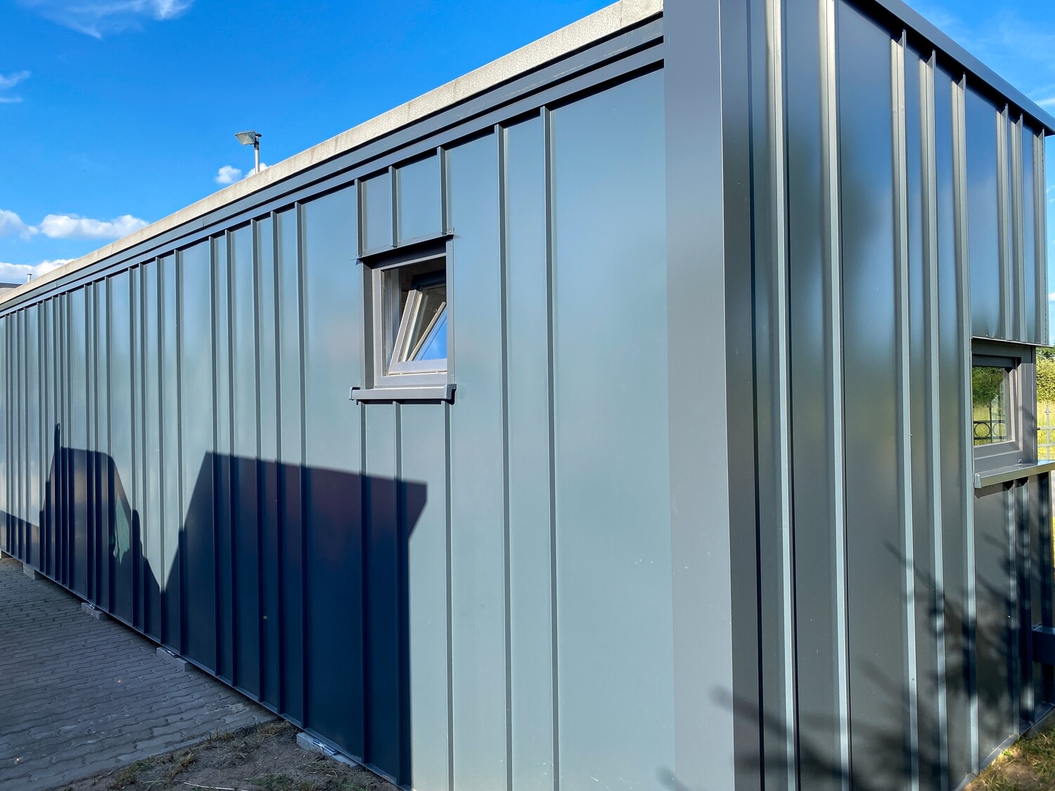 Längsseite in graugrüner Profilblechfassade, darin ein einzelnes gekipptes Fenster mit Fensterbank
