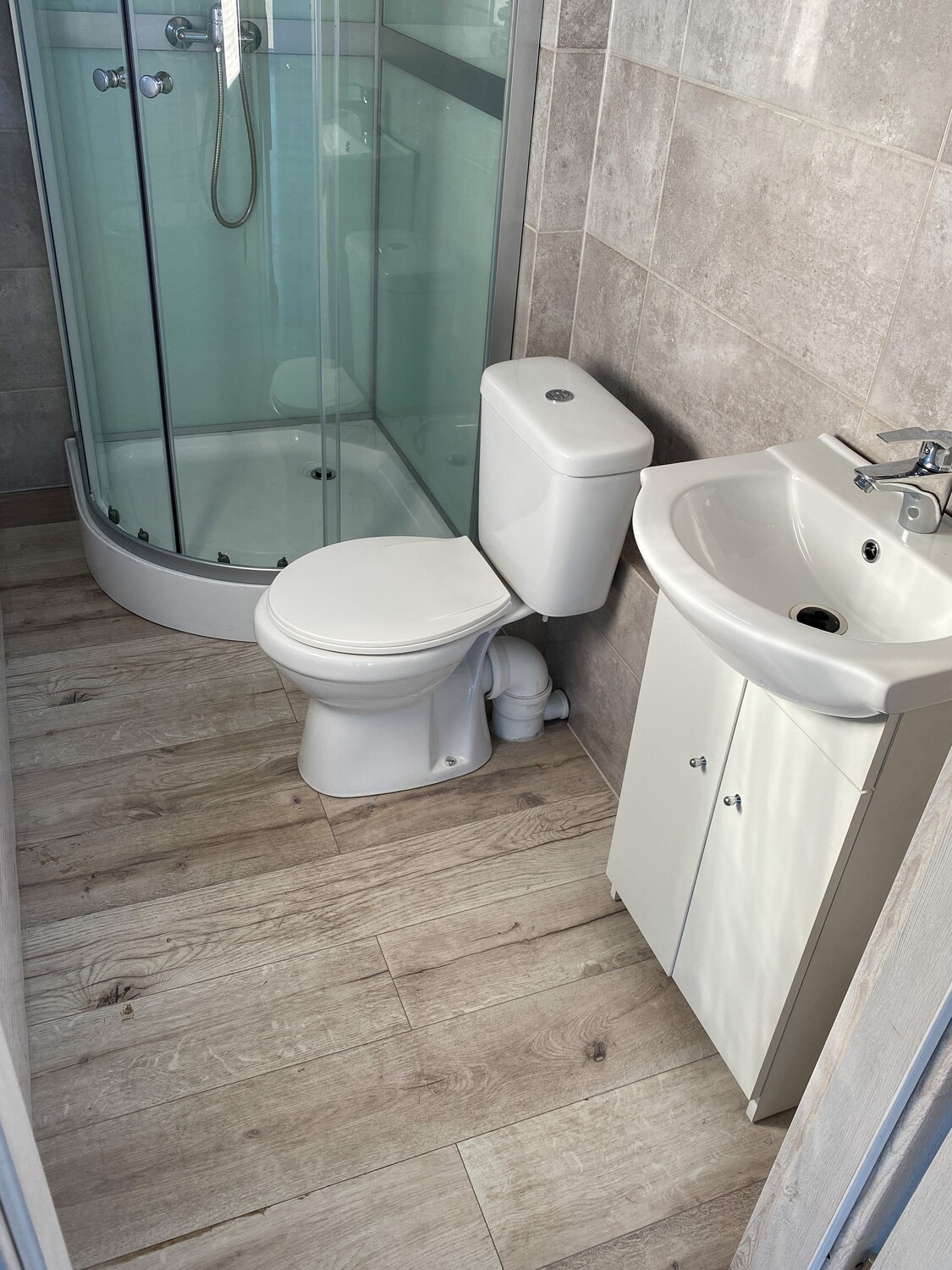 Detailaufnahme des Bads mit WC, Waschtischunterschrank und Eckdusche auf Boden in Holzoptik