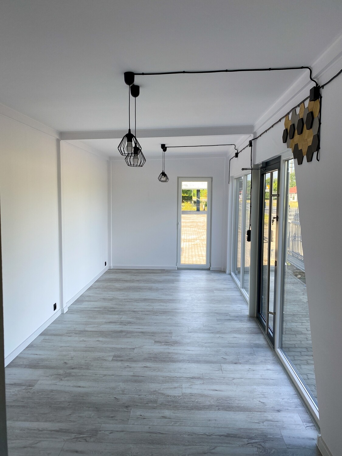 Leerer Wohnraum des Tiny House mit weißen Wänden, Vinylboden, Pendelleuchten und raumhoher Glasfront