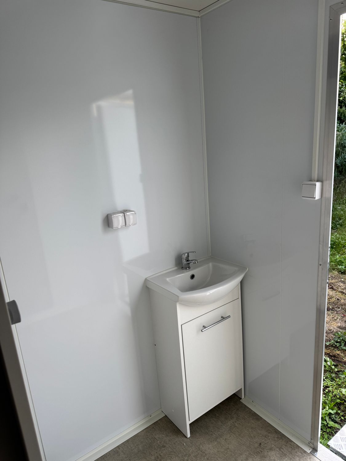 Waschplatz im WC-Anhänger mit Becken auf Unterschrank, Steckdosen und geöffneter Außentür