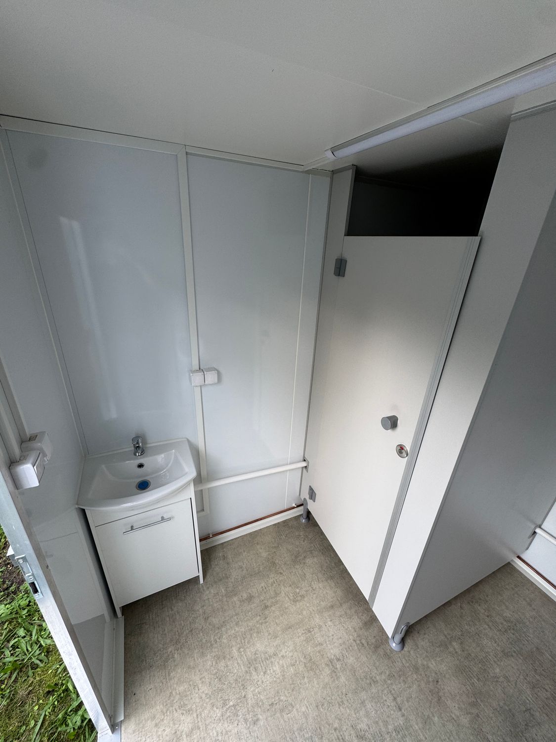 Eckperspektive auf Waschbecken mit Unterschrank und die offen stehende Kabinentür des Anhängers
