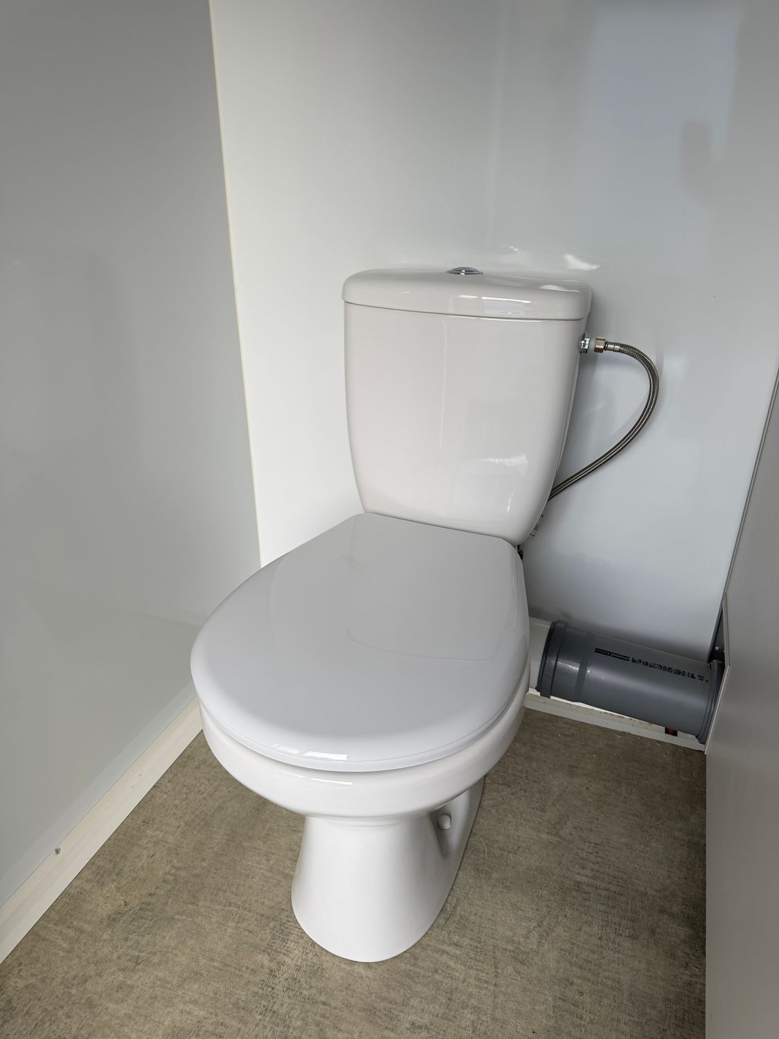 Detailaufnahme eines WCs mit Spülkasten, Anschlussschlauch und offen geführtem Abflussrohr