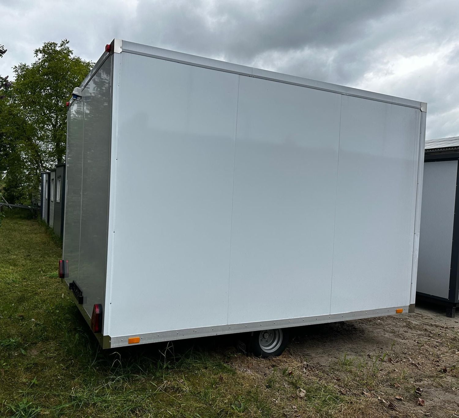 Rückansicht des WC-Anhängers mit Rückleuchten, seitlichen Reflektoren und Rad im Gras