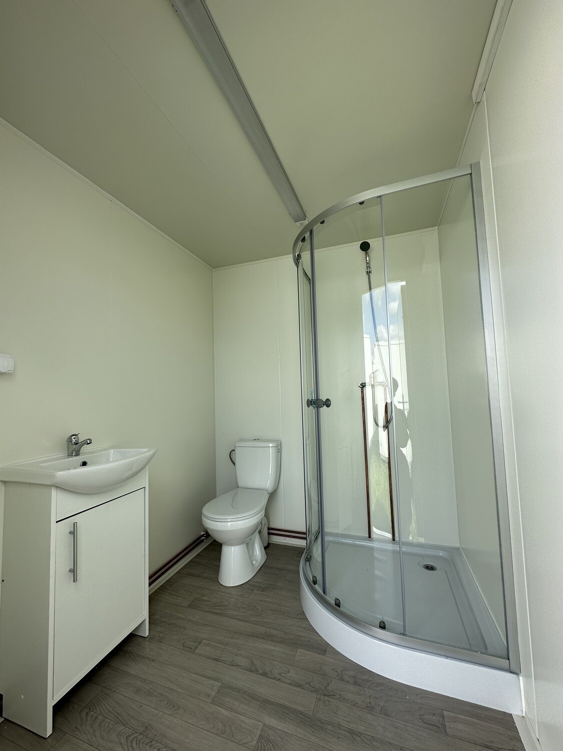 Innenansicht mit Waschtisch, WC und viertelrunder Duschkabine über Boden in Holzoptik