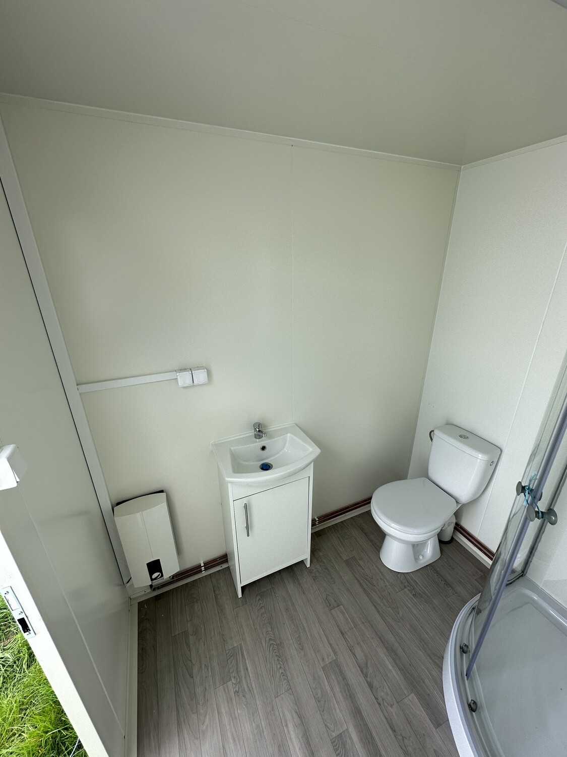 Blick in die Nasszelle: Waschtisch, Toilette, Handtuchhalter und weißes Wandgerät neben der Dusche