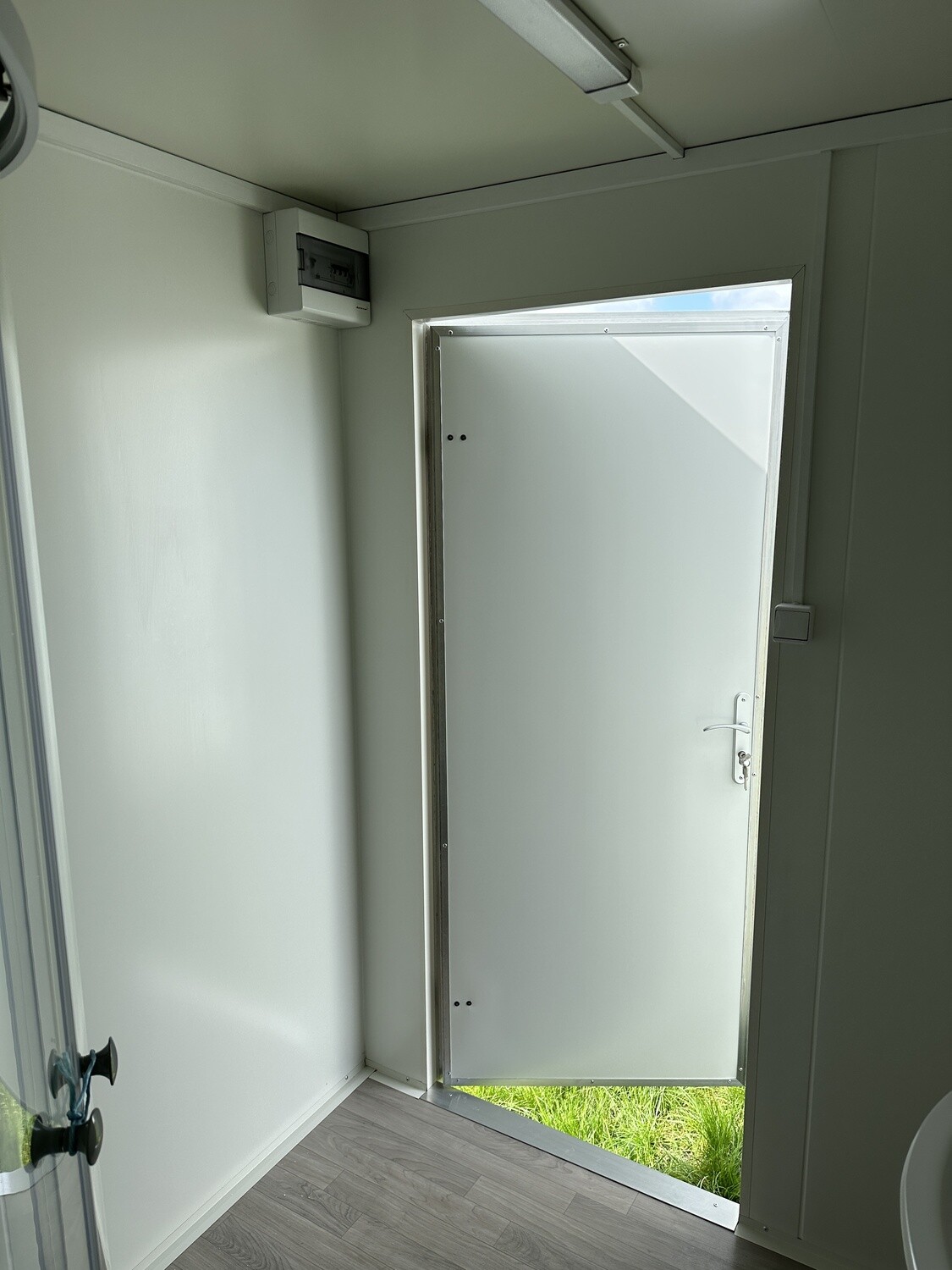 Geöffnete Eingangstür von innen gesehen, darüber ein Sicherungskasten an der hellen Wand