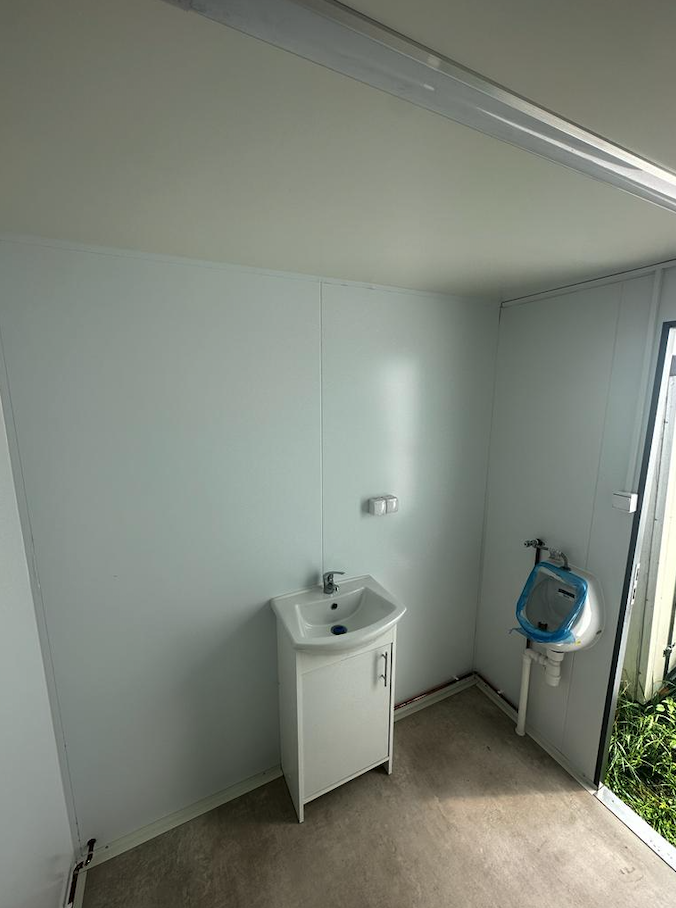 Herrenabteil mit Urinal, Waschbecken und geöffneter Tür, Blick auf helle Wandverkleidung