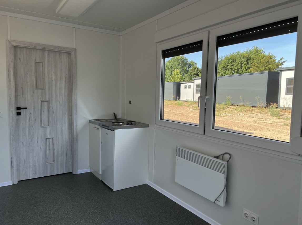 Blick auf die Küchenzeile mit Spüle, daneben die Holzdekor-Tür und ein Heizkörper unter dem Fenster